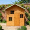 An angled view of a wooden two storey Cottage Playhouse with a central wooden door and multiple windows on a brick floor