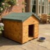 A front angle of a wooden dog kennel with a felt roof and access hole at the front on the structure, situated outside in a showroom on a brick floor