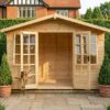 A wooden Georgian Summerhouse on the back wall of a wooden fence perimeter, with double doors and opening windows on a timber frame with a paving slabs path leading to the doors