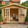 Wooden Georgian summerhouse with French doors open showing furnished interior with armchairs, on a paved patio with potted plants – Rutland Sheds