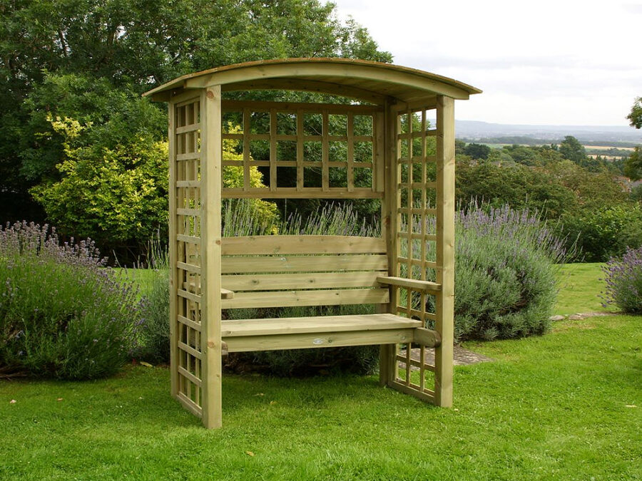A stylish wooden Northwood Arbour product situated infront of bushes and trees in a large country garden