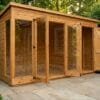 Wooden contemporary summerhouse exterior view with large bifold glass doors and adjacent side storage door closed, on a paved patio with rose borders – Rutland Sheds
